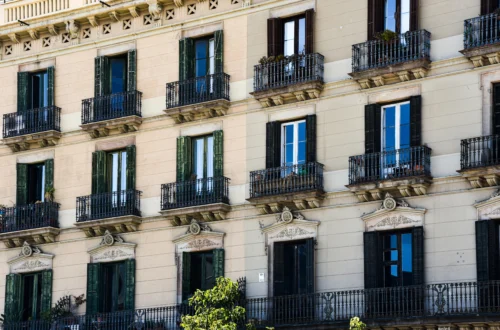 View of the façade of a classic residential building in Barcelona, featuring wrought-iron balconies, green and black shutters, and ornate architectural details