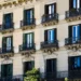 View of the façade of a classic residential building in Barcelona, featuring wrought-iron balconies, green and black shutters, and ornate architectural details