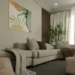 Elegant living room with a beige corner sofa, grey and brown cushions, a decorative throw, light wood coffee table, large window with white curtains, natural plant, and an abstract botanical-themed painting on the wall.