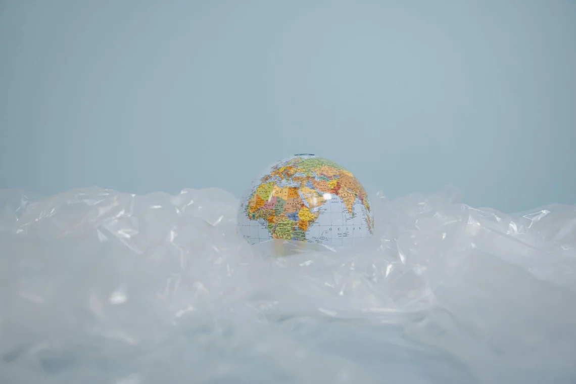 A globe partially covered by transparent plastic on a blue background, representing the global threat of plastic pollution.