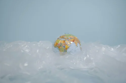A globe partially covered by transparent plastic on a blue background, representing the global threat of plastic pollution.