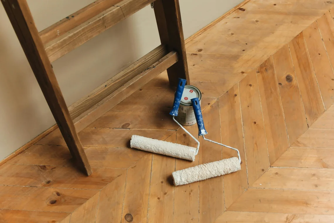 Two paint rollers and a paint can placed on a light wooden floor, ready for painting