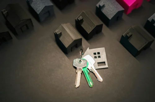 Keys on a figure of a house next to several models of houses, representing the sale or transfer of a property.
