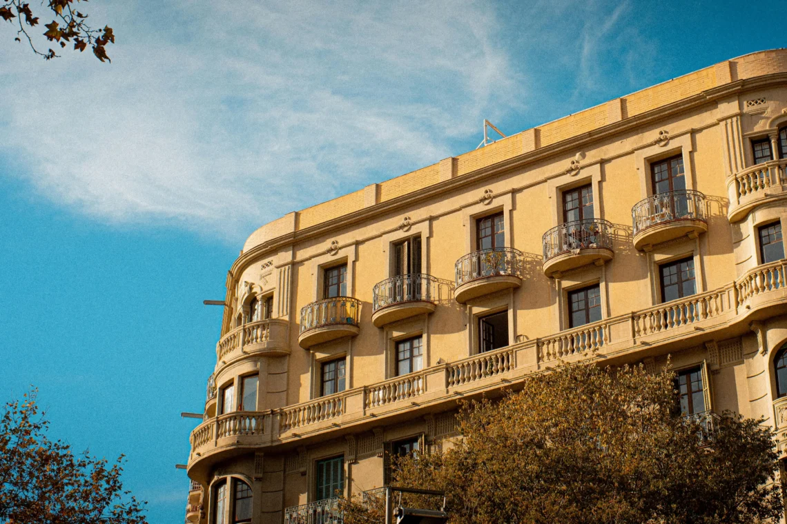 Fachada de un edificio clásico en Barcelona con balcones de hierro forjado bajo un cielo azul, representando los apartamentos legales en la ciudad