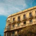 Fachada de un edificio clásico en Barcelona con balcones de hierro forjado bajo un cielo azul, representando los apartamentos legales en la ciudad